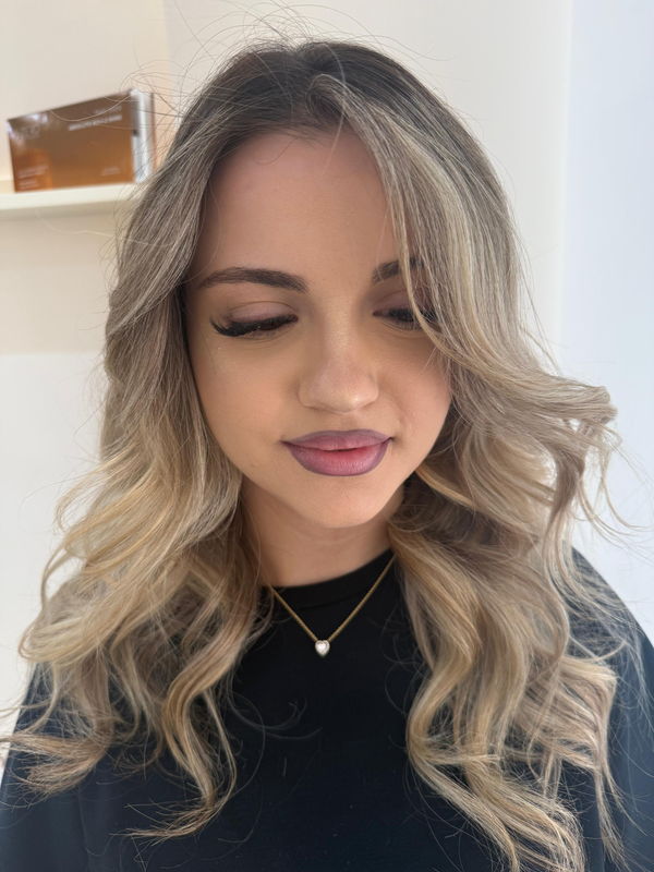 Kliente me make-up natyral dhe flokë bionde të stilizuara me onde të buta